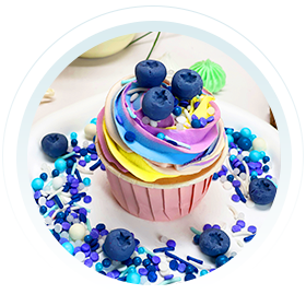 A beautifully decorated cupcake with colorful icing and blueberries, surrounded by various cake sprinkles and edible cake decoration candy, making it a delightful treat for any occasion.