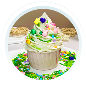 Delicious Easter-themed cupcake with white icing and colorful sprinkles, featuring bunny-shaped candies and speckled egg decorations, presented on a plate with additional festive cake decoration candy.